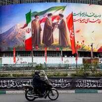 גבר רוכב על אופנוע ועובר ליד שלט המוצג בכיכר ואליאסר במרכז טהרן | AFP גבר רוכב על אופנוע ועובר ליד שלט המוצג בכיכר ואליאסר במרכז טהרן | AFP