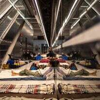 אישה משתמשת בטלפון נייד כשהיא שוכבת על מזרן בתחנת רכבת ששימשה כמקלט תת-קרקעי | אולימפיה דה מייסמונט / AFP אישה משתמשת בטלפון נייד כשהיא שוכבת על מזרן בתחנת רכבת ששימשה כמקלט תת-קרקעי | אולימפיה דה מייסמונט / AFP